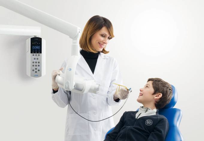 A smiling dentist using the Acteon SOPIX 2 dental sensor on a young patient